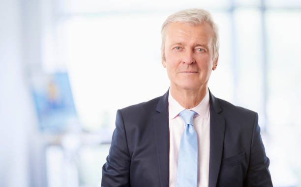 A senior sales manager standing at the office and looking at camera.